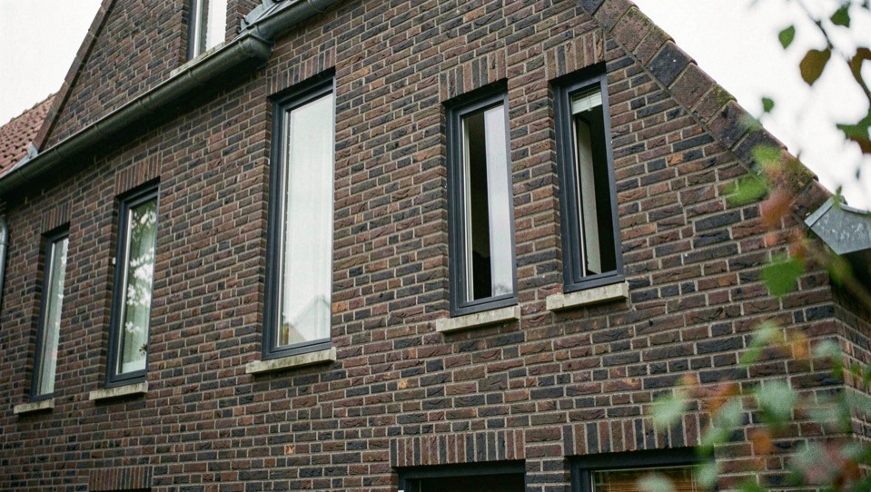 Gevel van een woning in donkere baksteen met hoge smalle raamopeningen en antracietkleurige kozijnen